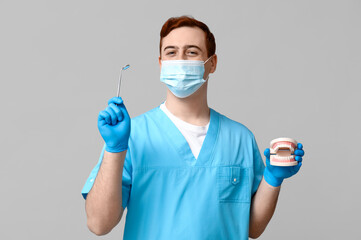 Male dentist in mask with jaw model and dental mirror on grey background. World Dentist Day