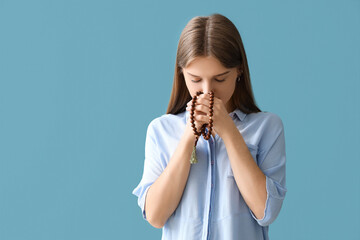Young woman praying with beads on blue background