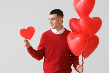 Handsome man with paper heart and balloons on light background. Valentine's Day celebration