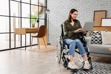 Happy young woman in wheelchair using laptop at home