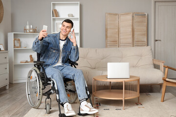 Happy young man in wheelchair with headphones using mobile phone at home