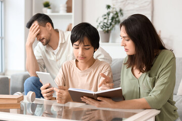 Teenage boy with tablet computer and his mother showing book at home. Family problem concept