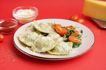 Plate of tasty ravioli with tomatoes and cheese on red background