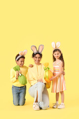 Happy mother and her little children with Easter gift eggs on yellow background