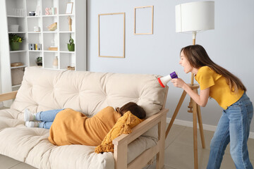 Little girl shouting into megaphone at her sleeping mother in room. April Fools' Day celebration