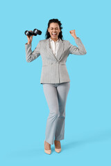 Happy young African-American businesswoman with binoculars on blue background