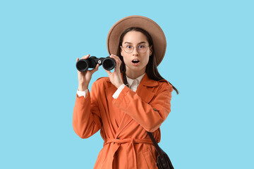 Shocked female detective with binoculars on blue background