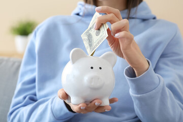 Woman putting money into piggy bank at home, closeup