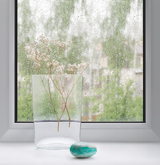 A glass vase on the background of a window with raindrops on the glass