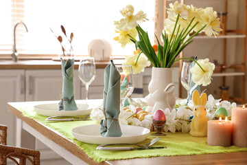 Festive table setting with vase of yellow tulips and Easter bunnies in stylish kitchen