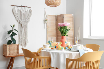 Festive table setting with vase of flowers, painted eggs and Easter bunnies in dining room