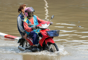 A moto-taxi with passenger drives through a flooded street, Bangkok, Thailand