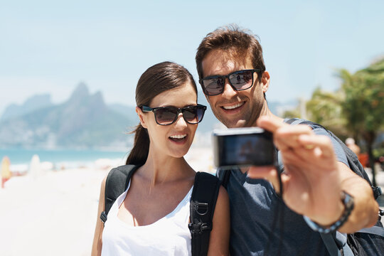 Couple, beach and camera for selfie on holiday with smile, sunglasses and outdoor for memory in summer. People, man and woman with photography by ocean for journey, vacation and sunshine in Italy