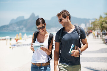 Couple, tourist and beach with map for guide on holiday, tour and travel for summer in Rio de Janeiro. Relationship, vacation and happy in seaside for trip in adventure, together and smile for break