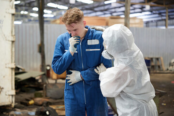 worker have a sick and coworker with personal protective equipment uniform(PPE) helping him in the factory - obrazy, fototapety, plakaty