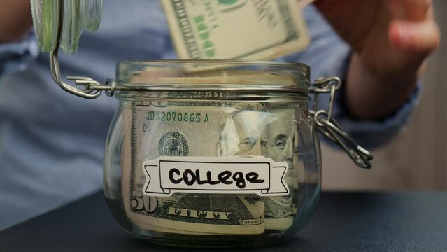 Female hands add money to Glass jar full of American currency dollars cash banknote with text COLLEGE. Preparation saving money. Moderate consumption and economy. Collecting money
