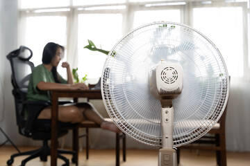 Sunny summer in front of the working fan, suffering from the summer heat. Unhappy Asian woman...