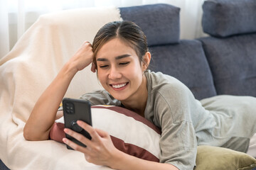 Portrait young Asian woman with casual lifestyle  lying on sofa and texting on mobile phone