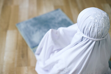 High angle rear view of muslim woman raising hand praying while sitting on prayer mat