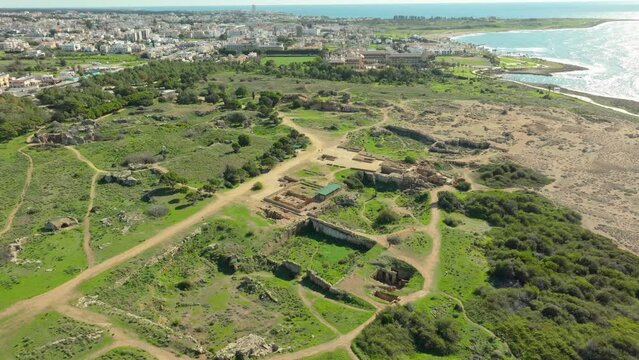 Aerial view sprawling archaeological site of the Tombs of the Kings in Paphos, Cyprus, nestled between the cityscape and the coast, highlighting the ancient ruins amid modern urban development
