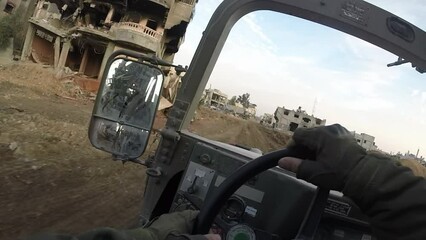 Israeli soldier driving a Humvee  down a road through the destroyed streets of Gaza