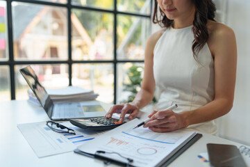 Asian female finance staff is pressing a calculator to calculate company sales and profit to report...