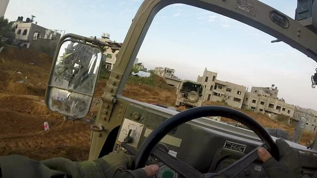 Two Israeli Humvees driving on road through destroyed city streets in Gaza
