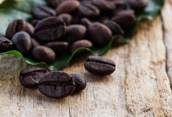 Coffee beans and green leaf on wooden background