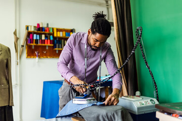 Young male African American tailor ironing shirt in his atelier.