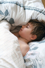 Cute little toddler boy is sleeping with beige plaid at home. Bedtime, napping