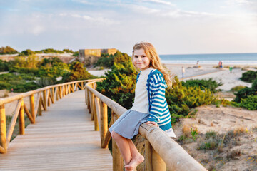 Fototapeta na wymiar Adorable happy smiling little girl on beach vacation at sunset. Handsome cute preschool child with long blond hairs having fun on family vacations.