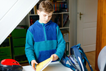 School kid boy getting ready in the morning for school. Healthy child filling satchel with books,...