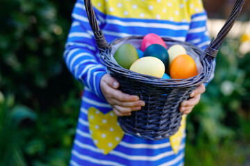 Close-up of of hands of toddler holding basket with colored eggs. Child having fun with traditional...