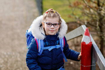 Cute little girl o the way to school. Healthy happy child with eyeglasses walking to primary...