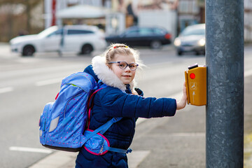 Obraz premium Cute little girl o the way to school. Healthy happy child with eyeglasses walking to primary school. Smiling child with schoolbag on the city street, outdoors. Back to school.