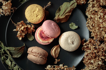 Macaroons with dried flowers on a black plate.