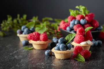Small tartlets with fresh raspberries and blueberries on a black background.