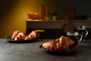 Fresh baked croissants and black coffee on a kitchen table.