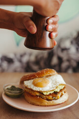 Close-up of someone grinding pepper onto a fried egg sandwich on a pink plate