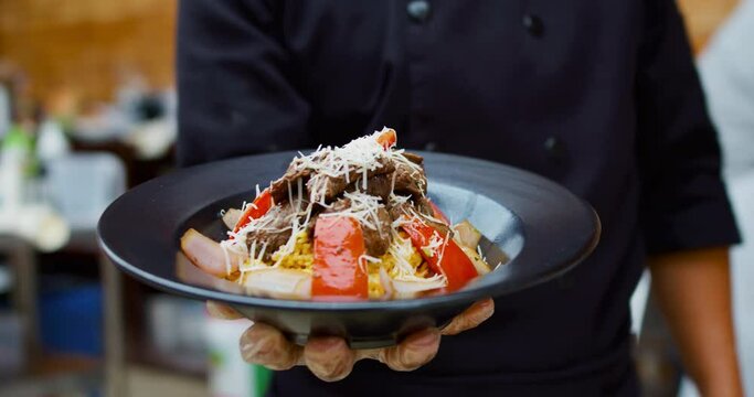 Amazing slow motion and zoom in shot of the presentation of a Peruvian dish called Lomo Saltado while a cook holds it in one hand