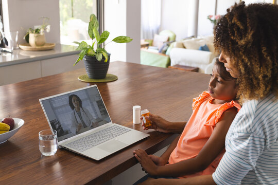 Biracial mother and daughter at home, consulting a doctor online