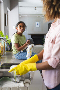 Biracial daughter helps with dishes at home for daughter, with copy space