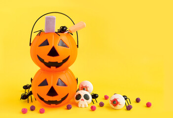 Halloween Jack o Lantern plastic pumpkin bucket, candies eyes, lolipop and spiders in the jack basket on yellow background. Scary halloween's
