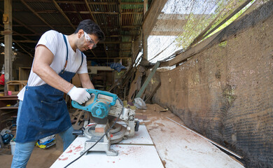 Young carpentry using a power miter saw to cut a piece of wood. Atmosphere in a workshop or outdoor...