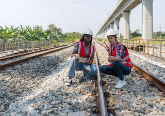 Rail transportation engineer in safety vest and hardhat check the neatness of the railway track while holding walkie-talkie and tablet computer.