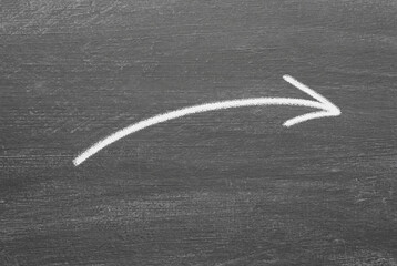 Hand drawn Arrow in white chalk on a blackboard background. Arrow drawn with white chalk.