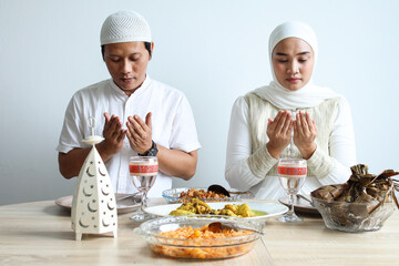 Muslim couple praying together before eat special dish on Eid moment, hand raised and bow head. Eid Mubarak ramadan celebration.