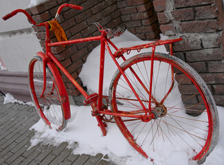 An old bike of bright red color abandoned on a city street. An art installation in the form of an old, forgotten, broken bicycle.