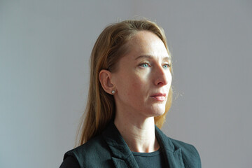 Portrait in profile of an adult attractive young woman in a black suit on a white background with a stern expression on her face