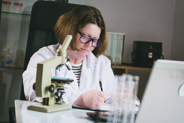 An adult Caucasian scientist woman in glasses writes down the results of her work
